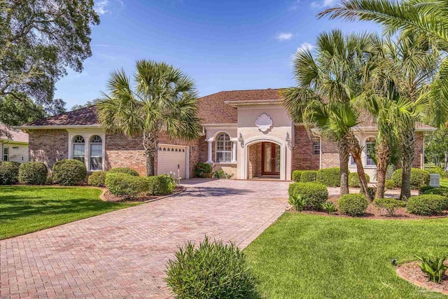 mediterranean / spanish house featuring decorative driveway, a front lawn, a garage, and brick siding