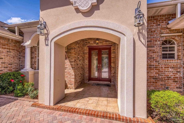 property entrance with stucco siding, brick siding, and french doors