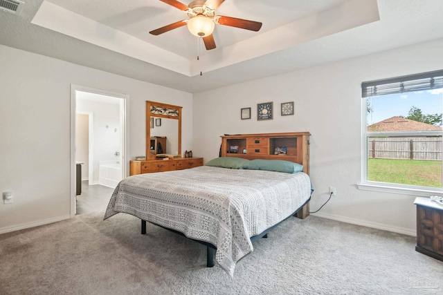 carpeted bedroom featuring a tray ceiling, ceiling fan, and ensuite bath