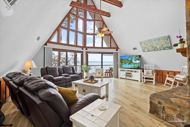 living room with high vaulted ceiling, wooden walls, light hardwood / wood-style floors, beamed ceiling, and ceiling fan