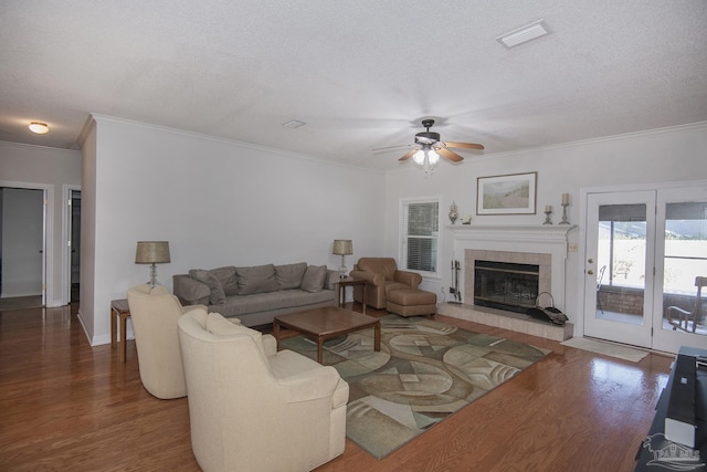 living room with ceiling fan, dark wood-type flooring, crown molding, a textured ceiling, and a tiled fireplace