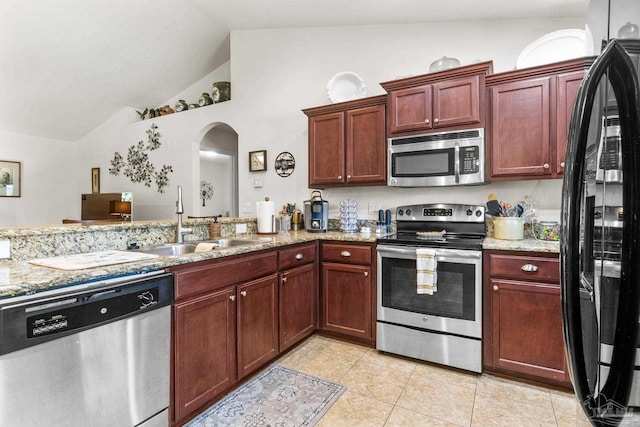 kitchen with stainless steel appliances, arched walkways, vaulted ceiling, light stone countertops, and light tile patterned floors