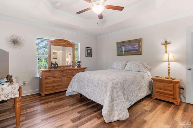bedroom with baseboards, crown molding, wood finished floors, and a raised ceiling