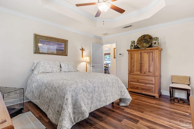bedroom with a tray ceiling, dark wood-style floors, visible vents, a ceiling fan, and crown molding
