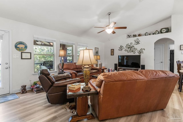 living area with arched walkways, light wood finished floors, lofted ceiling, and a ceiling fan