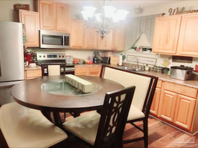 kitchen featuring appliances with stainless steel finishes, an inviting chandelier, light brown cabinetry, hanging light fixtures, and light hardwood / wood-style flooring