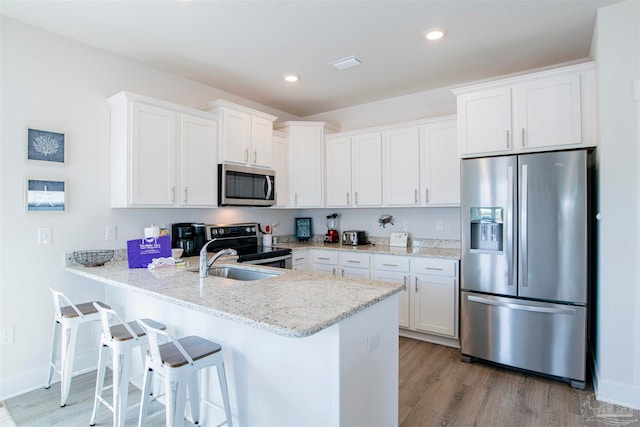 kitchen with white cabinets, kitchen peninsula, stainless steel appliances, light stone countertops, and light hardwood / wood-style floors