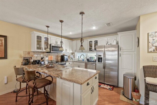 kitchen with appliances with stainless steel finishes, tasteful backsplash, light stone counters, kitchen peninsula, and light hardwood / wood-style floors