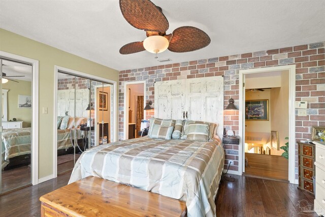 bedroom featuring two closets, dark hardwood / wood-style flooring, brick wall, and ceiling fan