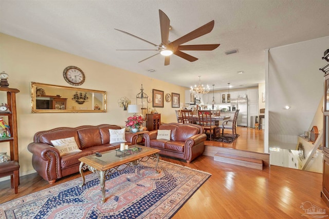 living room featuring ceiling fan with notable chandelier, a textured ceiling, and light hardwood / wood-style flooring