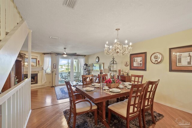 dining space with a fireplace, light wood-type flooring, ceiling fan with notable chandelier, and a textured ceiling