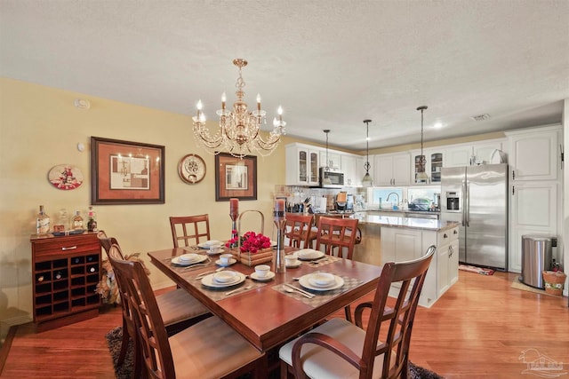 dining space featuring a notable chandelier, sink, a textured ceiling, and light wood-type flooring