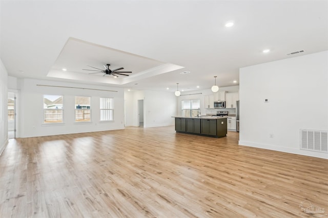 unfurnished living room with ceiling fan, light wood-type flooring, and a tray ceiling