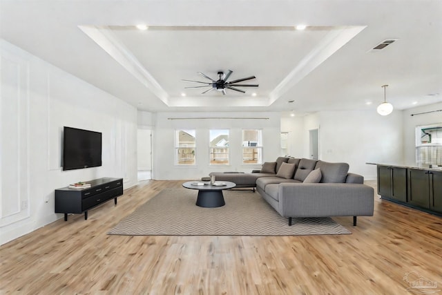 living room with a tray ceiling, light hardwood / wood-style flooring, and a healthy amount of sunlight