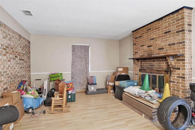 rec room featuring wood finished floors, visible vents, a textured ceiling, and a fireplace