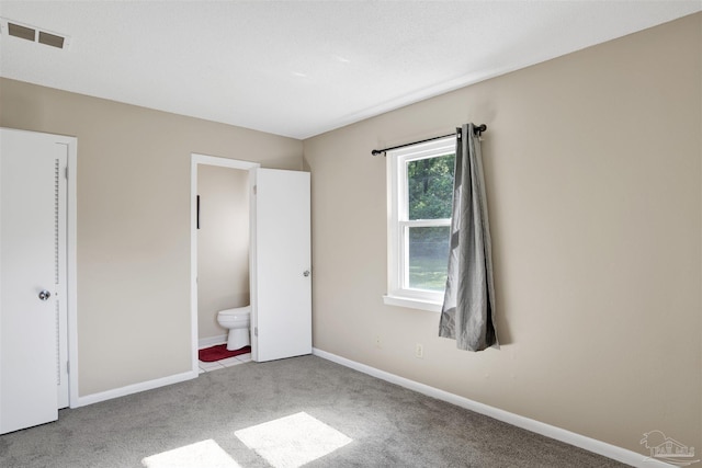 unfurnished bedroom with baseboards, visible vents, carpet floors, and connected bathroom