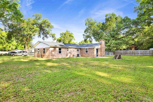 rear view of property featuring central air condition unit, a chimney, a lawn, a fenced backyard, and brick siding