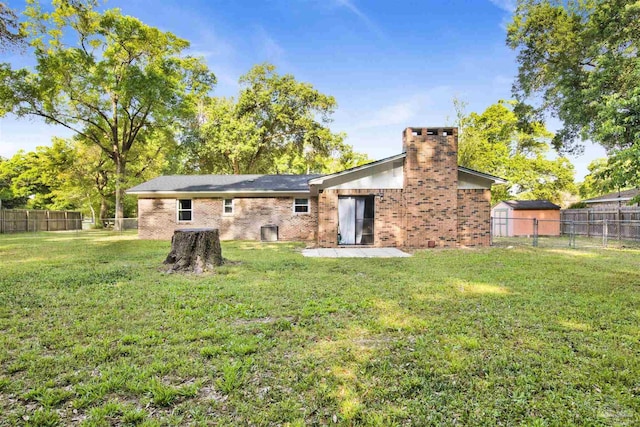rear view of house featuring a patio area, a lawn, a chimney, a fenced backyard, and brick siding