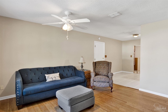 living area featuring baseboards, a ceiling fan, wood finished floors, and a textured ceiling