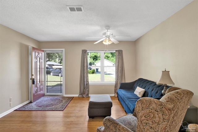living area featuring light wood finished floors, a textured ceiling, baseboards, visible vents, and a ceiling fan