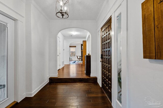 hallway with ornamental molding, dark hardwood / wood-style flooring, a textured ceiling, and a notable chandelier