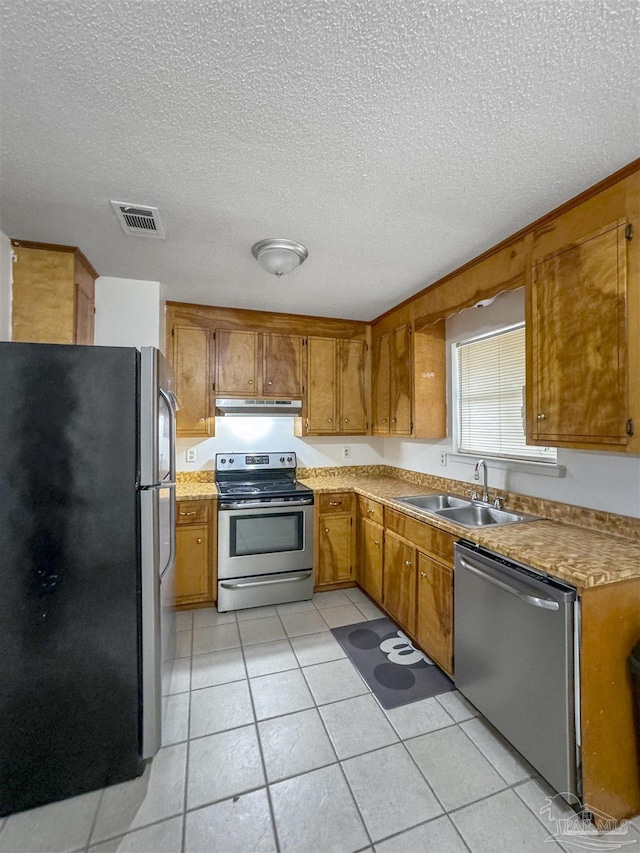 kitchen with appliances with stainless steel finishes, sink, a textured ceiling, and light tile patterned flooring