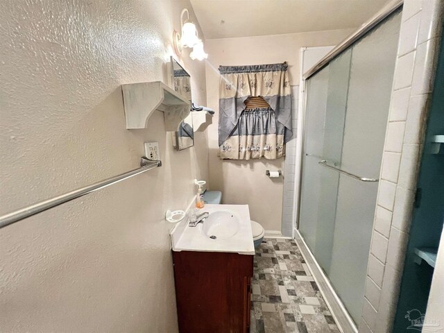 bathroom featuring tile patterned flooring, a shower with shower door, toilet, and vanity