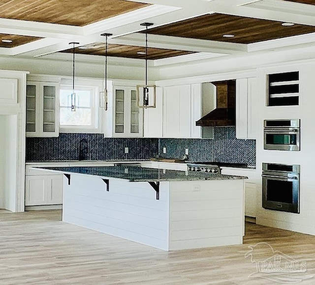 kitchen with a kitchen breakfast bar, white cabinetry, and wall chimney range hood