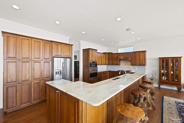 kitchen featuring dark wood-type flooring, a breakfast bar, a sink, appliances with stainless steel finishes, and brown cabinets