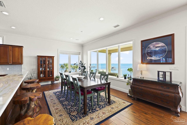 dining space featuring dark wood-type flooring, a water view, visible vents, and crown molding