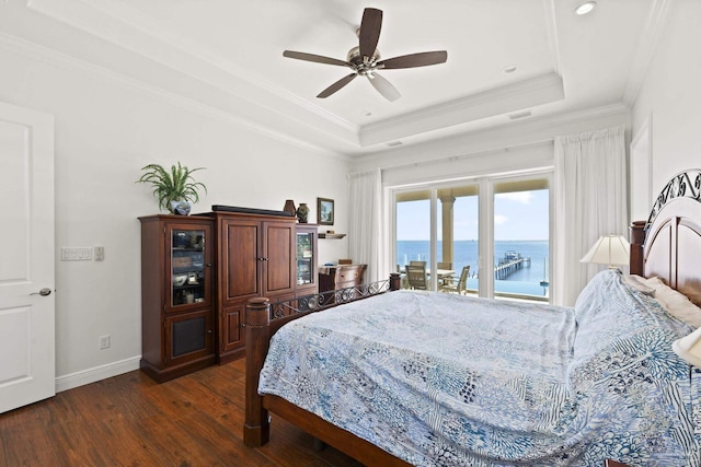 bedroom featuring a tray ceiling, dark wood-style flooring, crown molding, a water view, and baseboards