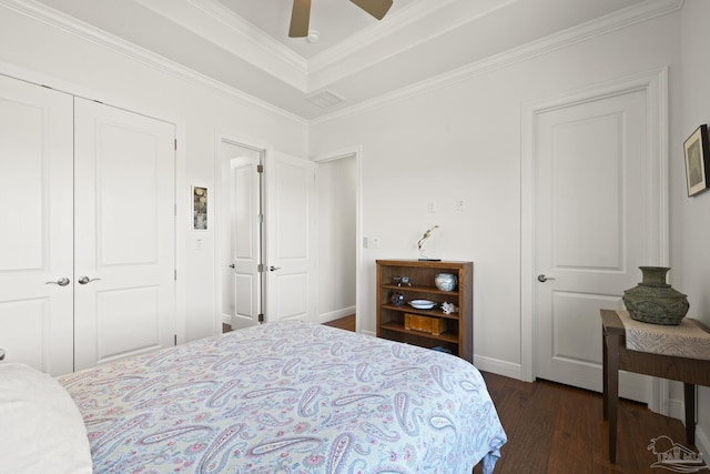 bedroom featuring ceiling fan, dark wood-style flooring, a tray ceiling, crown molding, and a closet