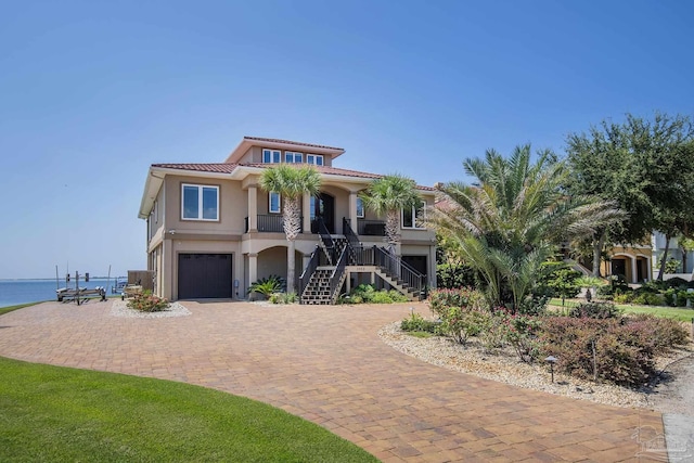 view of front of house featuring a tiled roof, a water view, stairs, decorative driveway, and stucco siding