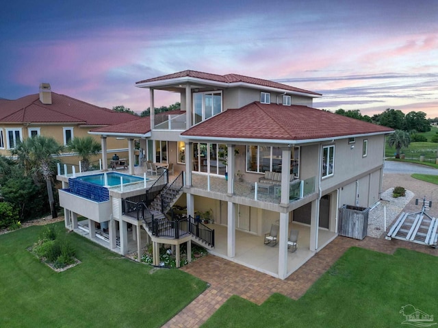 back house at dusk with a patio area, a balcony, and a yard