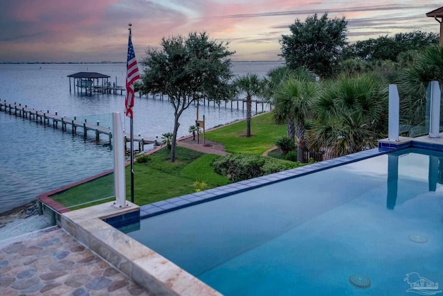 pool at dusk with a lawn, a water view, and a dock