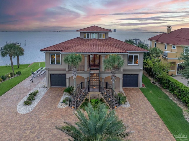 mediterranean / spanish-style home featuring a lawn, a porch, a water view, and a garage