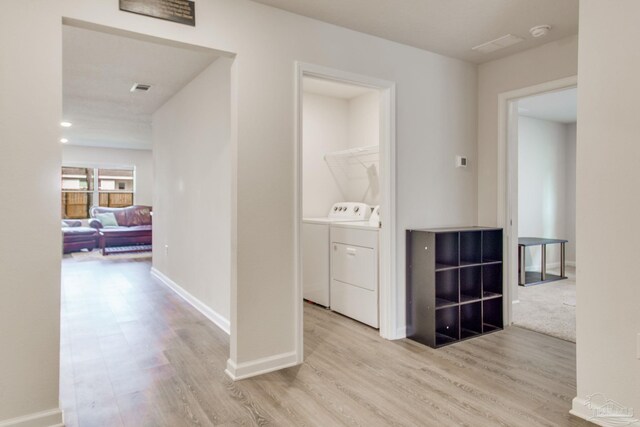 hallway with light wood-style floors, visible vents, washer and clothes dryer, and baseboards