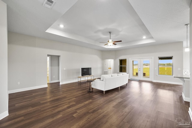 living area with a raised ceiling, baseboards, visible vents, ceiling fan, and dark wood-type flooring