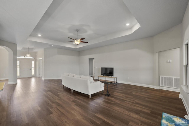 unfurnished living room with a raised ceiling, dark wood-style flooring, arched walkways, and visible vents