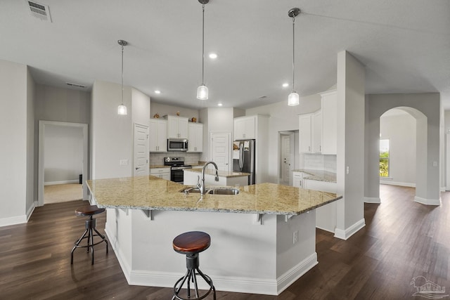kitchen with a spacious island, a sink, appliances with stainless steel finishes, visible vents, and arched walkways