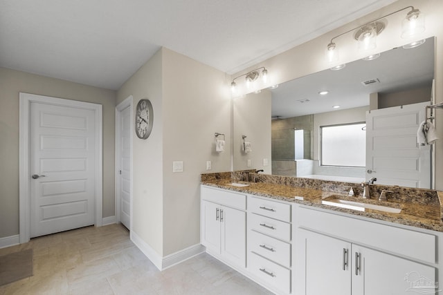 full bathroom featuring visible vents, baseboards, double vanity, a tile shower, and a sink