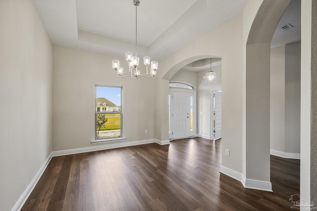 foyer featuring a tray ceiling, baseboards, arched walkways, and dark wood finished floors