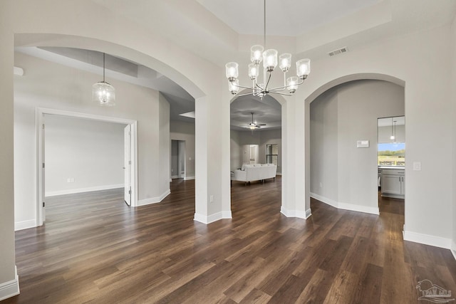 unfurnished dining area with a tray ceiling, dark wood-type flooring, baseboards, arched walkways, and visible vents