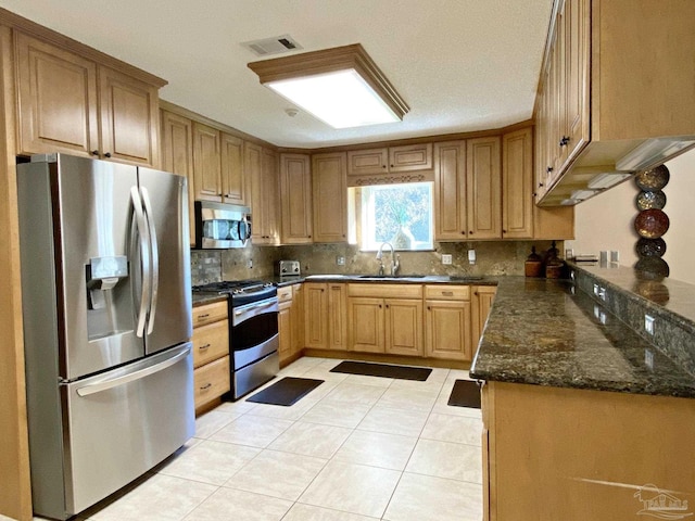 kitchen featuring sink, light tile patterned floors, dark stone countertops, stainless steel appliances, and decorative backsplash