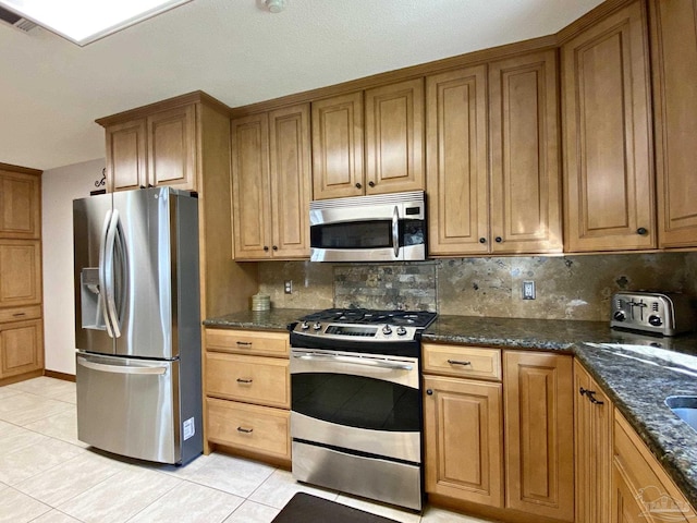 kitchen with tasteful backsplash, appliances with stainless steel finishes, light tile patterned flooring, and dark stone countertops