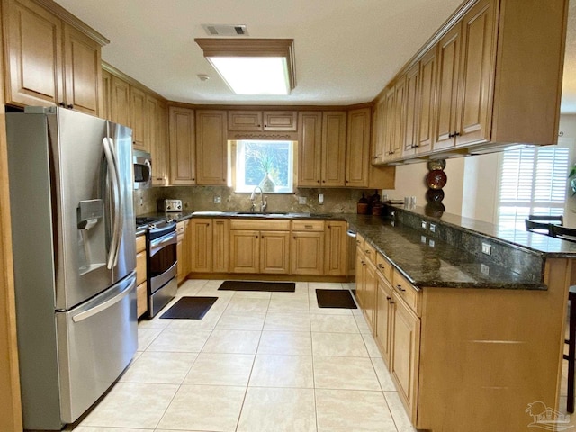 kitchen featuring light tile patterned flooring, sink, dark stone countertops, kitchen peninsula, and stainless steel appliances