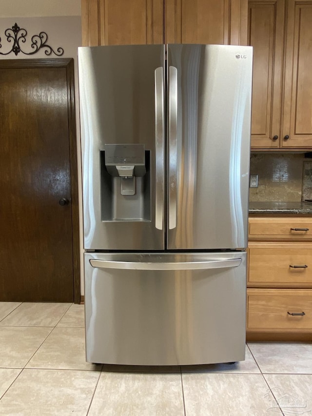 kitchen featuring stainless steel refrigerator with ice dispenser, light tile patterned floors, backsplash, and dark stone counters