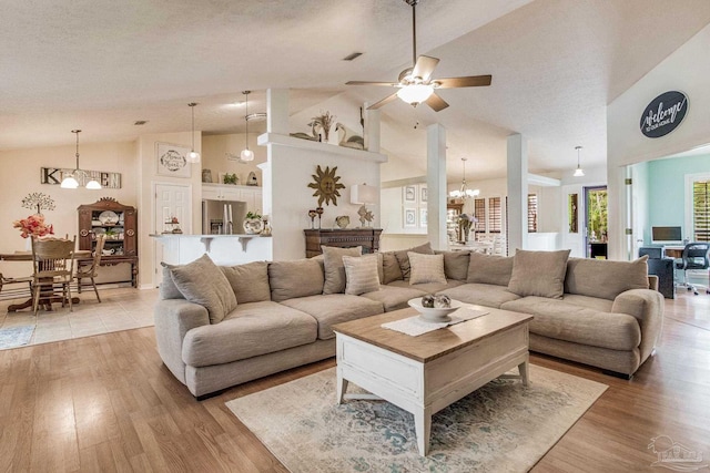 living room featuring ceiling fan with notable chandelier, light hardwood / wood-style floors, a textured ceiling, and high vaulted ceiling