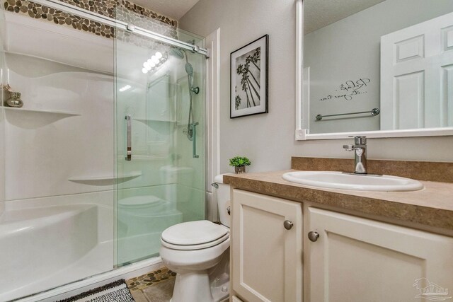 bathroom featuring tile patterned floors, a textured ceiling, toilet, vanity, and a shower with shower door