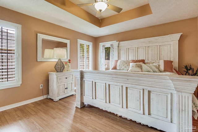 bedroom with ceiling fan, a raised ceiling, and light wood-type flooring